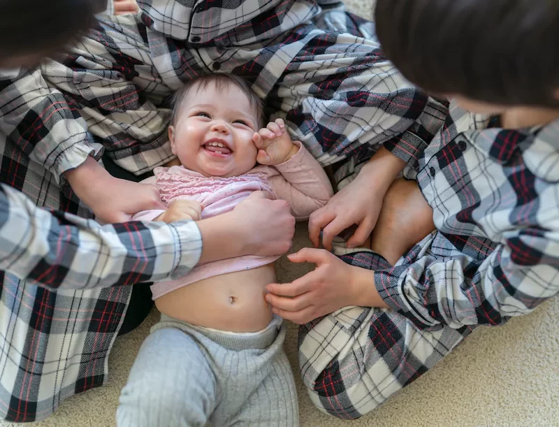 A group of people playing with a baby on the floor.