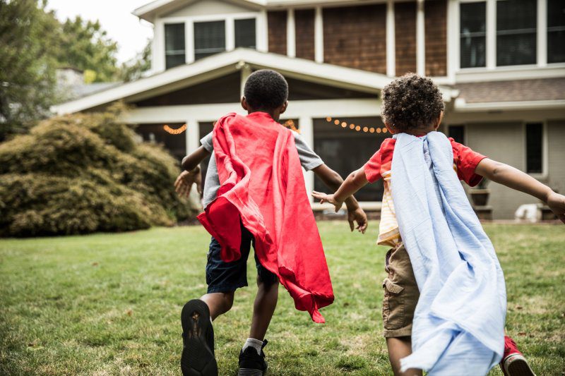 Two boys dressed as superheroes running in front of a house.