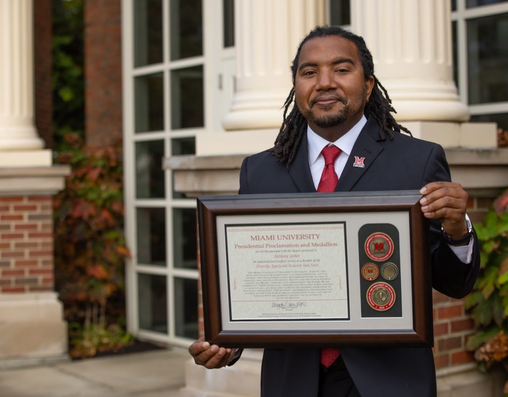 A man in a suit holding a framed certificate.