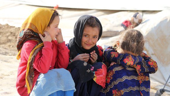 A group of young girls are sitting on the ground in front of tents.