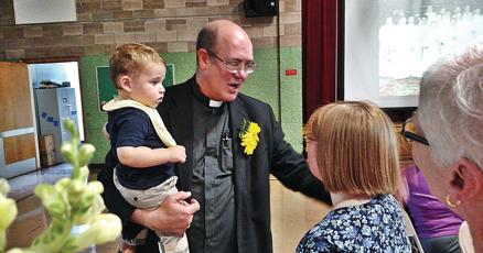 A priest is holding a child in front of a group of people.