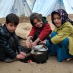 Iraqi refugee children cook in front of tents.