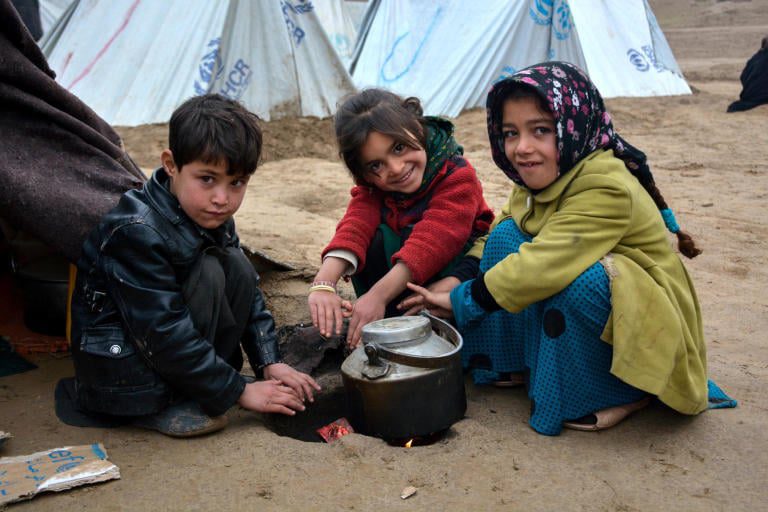 Iraqi refugee children cook in front of tents.