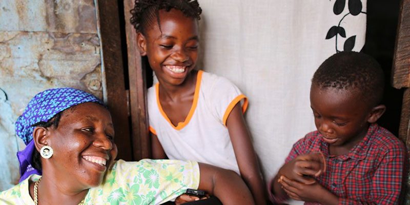 A woman holding a cell phone in front of a group of children.