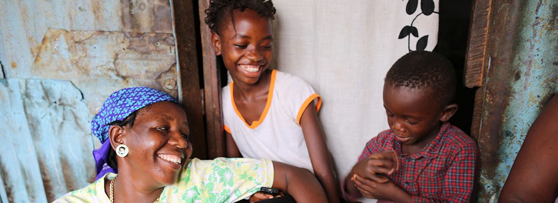 A woman holding a cell phone in front of a group of children.